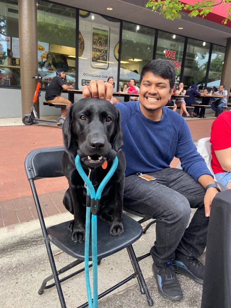 Student with his dog. The dog is sitting on a chair and  holding a leash in his mouth.