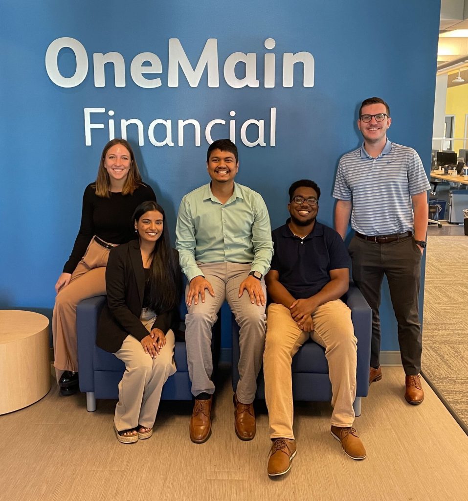 five students in front of OneMain Financial sign in an office
