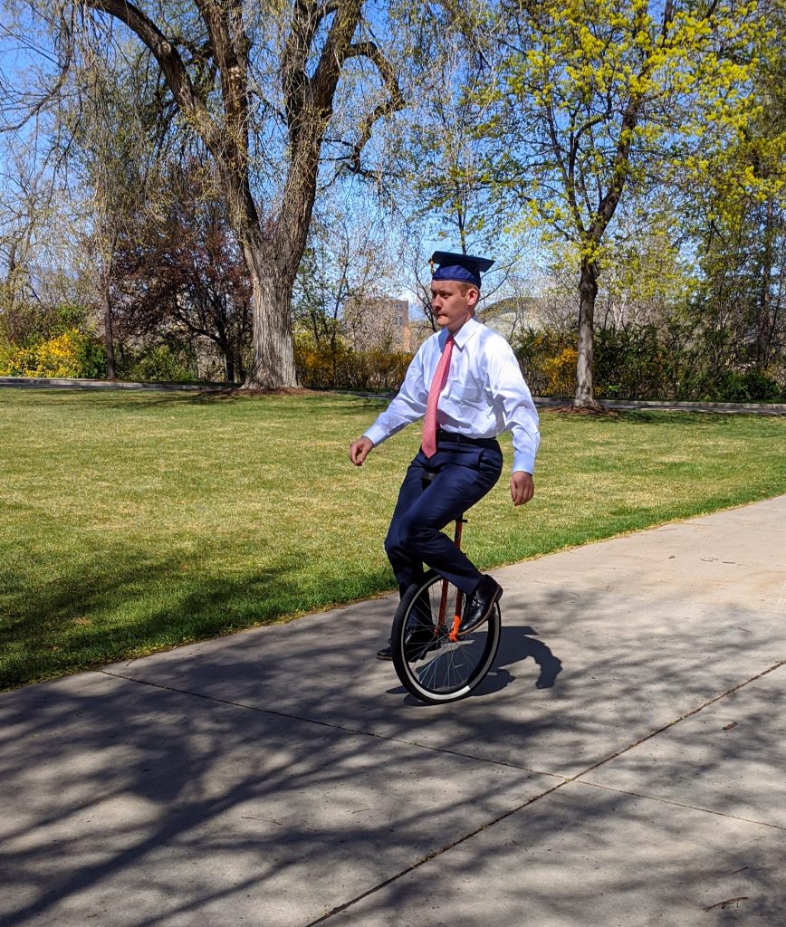 Man riding unicycle with graduation cap on
