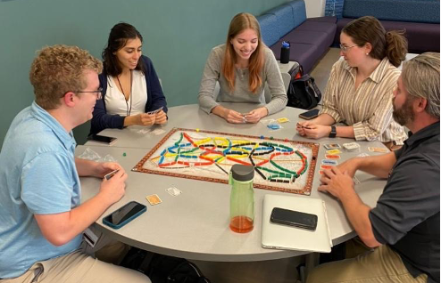 Group of five people sitting at a round table playing board games.