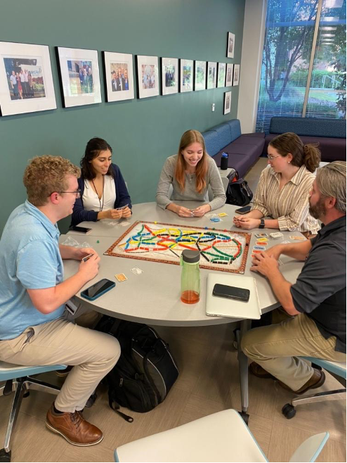 Five people at round table playing a board game.