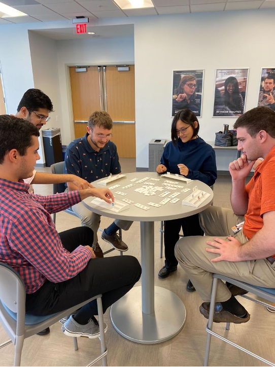 Five people at a tall round table playing board games
